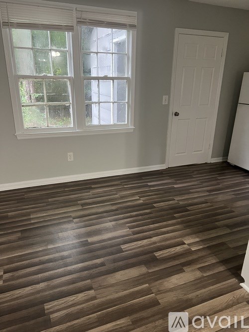 A room with a white door and a window with a view of trees and a building outside.