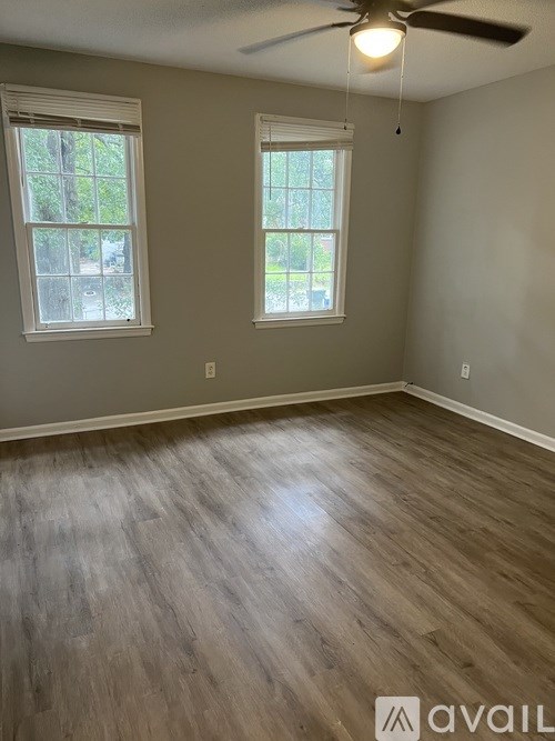 A room with wooden flooring and two windows.