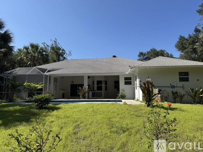 A house with a grey roof and a white fence is surrounded by greenery.