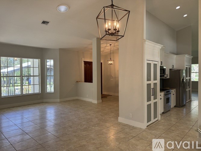 A spacious kitchen with white cabinets and a black chandelier.