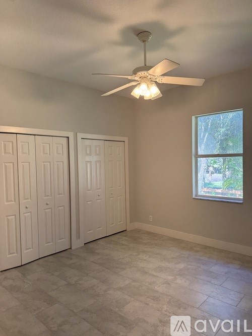 A room with a ceiling fan and a window with a view of trees.