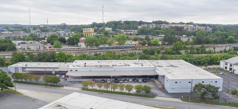 A large industrial building with a grey roof is surrounded by a parking lot.