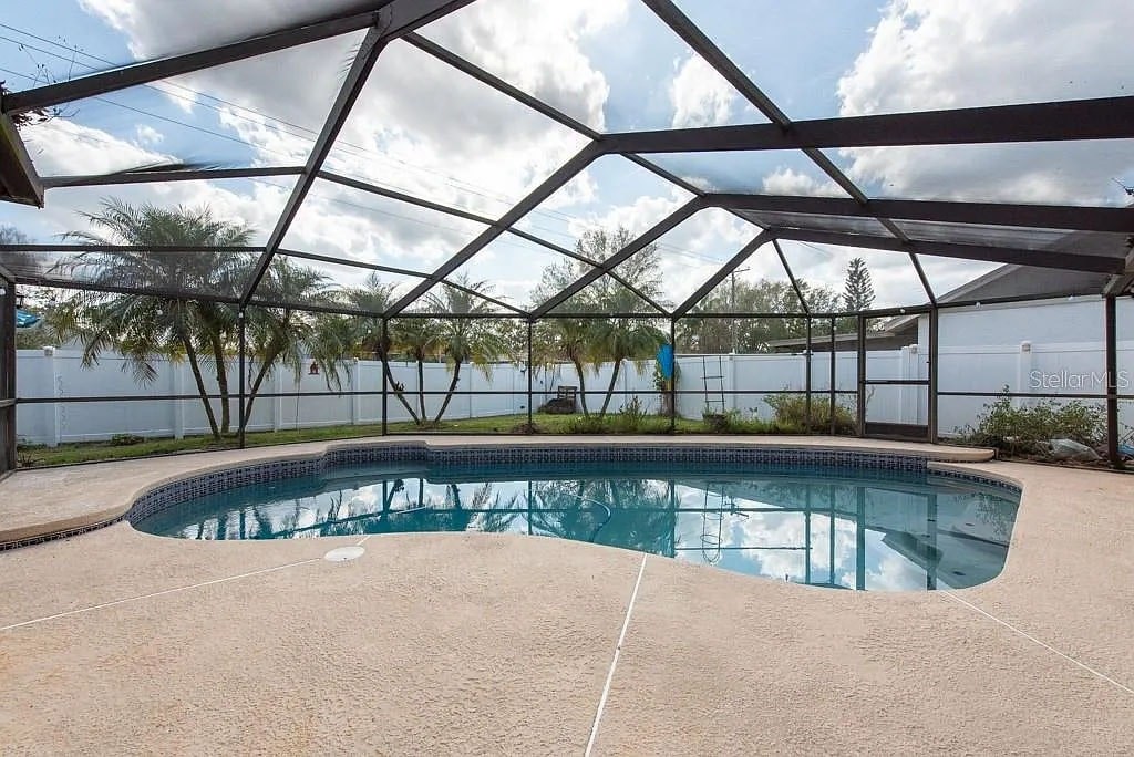 A pool under a metal roof with trees in the background.