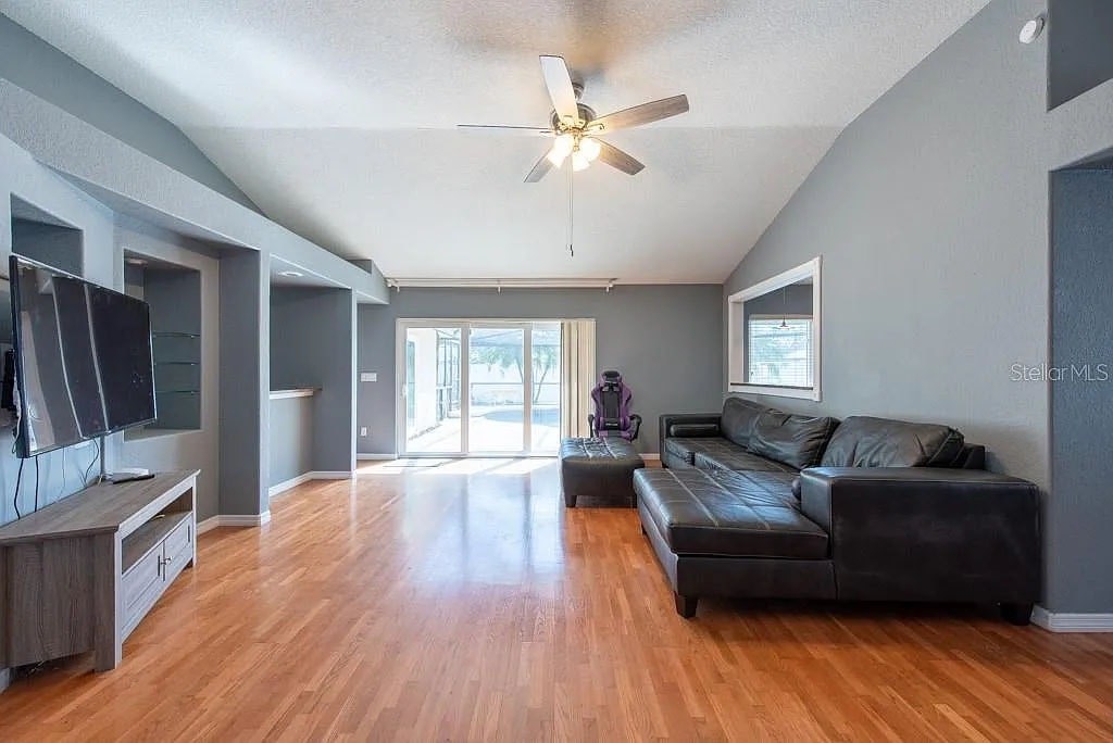A living room with a black leather couch and wooden floors.