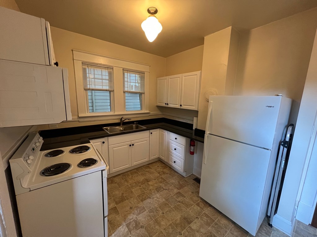A kitchen with white appliances and black countertops.