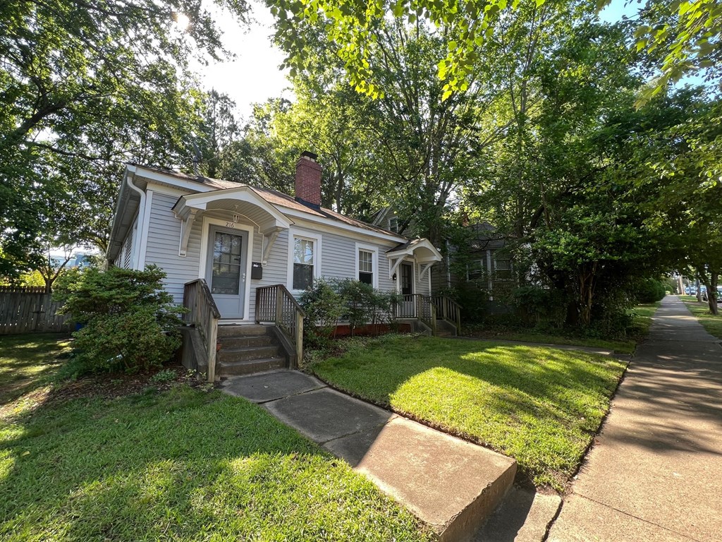 A white house with a brown roof is surrounded by green trees.
