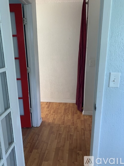 A room with a red door and a wooden floor.