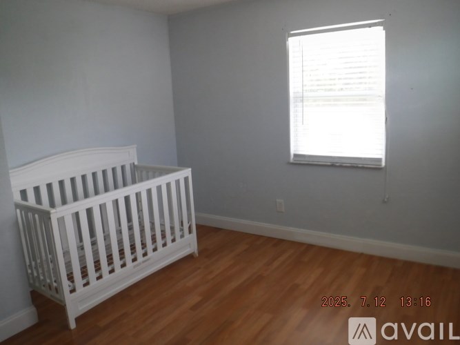 A white crib sits in a room with wooden floors and a window.