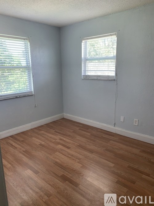 A room with wooden flooring and two windows.