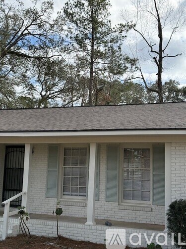 A white house with a grey roof and a tree in front.