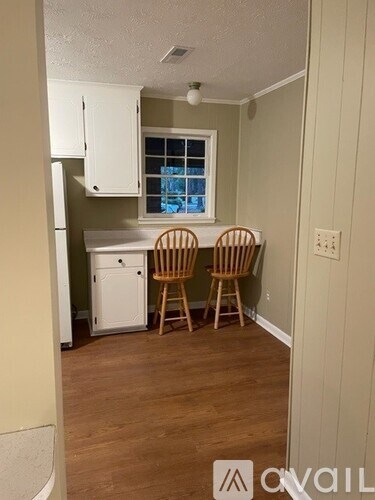 A kitchen area with a white refrigerator, a white cabinet, and two wooden chairs.