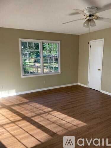A room with a ceiling fan and a window showing a view of trees and a lawn.