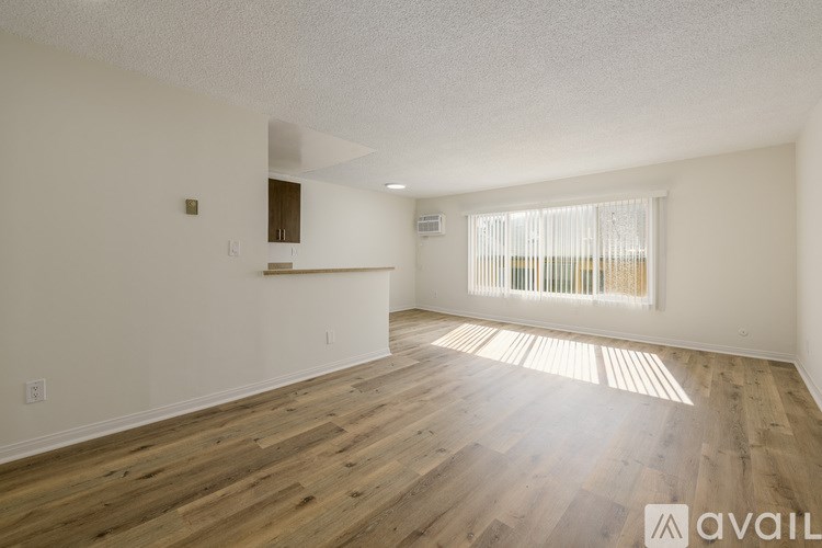 A spacious room with wooden flooring and a window with blinds.