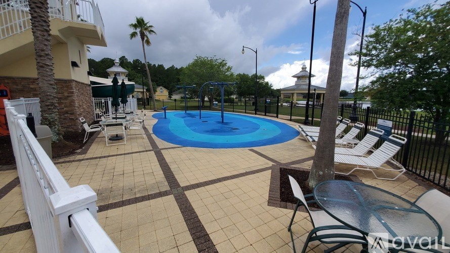 A pool area with a blue pool, white lounge chairs, and a white fence.