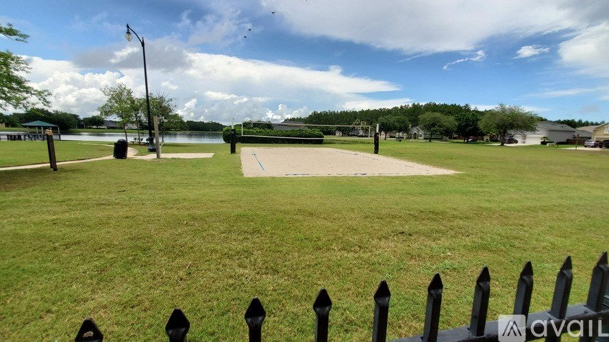 A black fence surrounds a green field with a lake in the background.