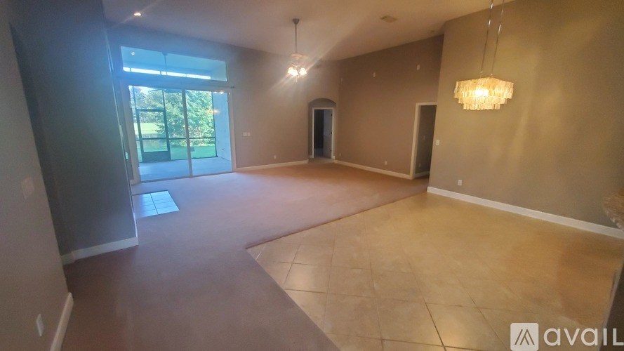 A spacious room with a large window and a chandelier hanging from the ceiling.