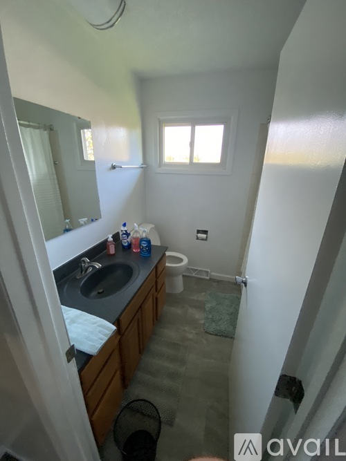 A bathroom with a sink, mirror, toilet, and a window.