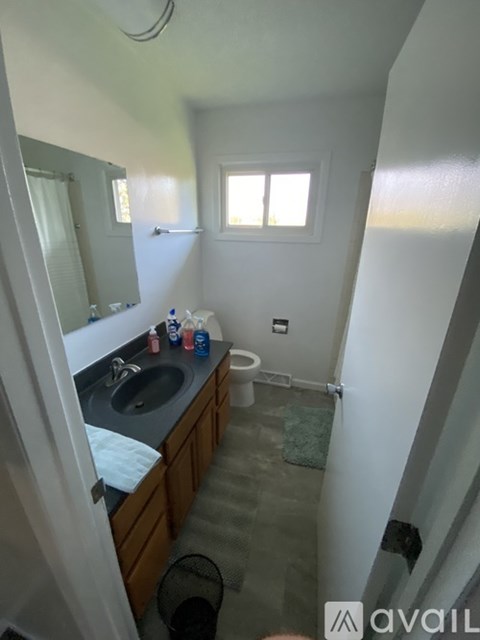 A bathroom with a sink, mirror, toilet, and a window.