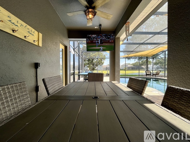 A wooden table is in the middle of a room with a television and a pool outside.
