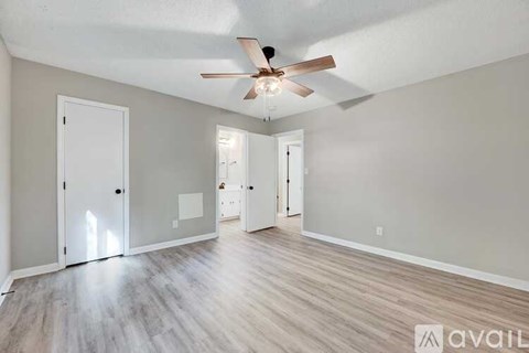 A spacious room with a ceiling fan and light, hardwood floors, and white walls.