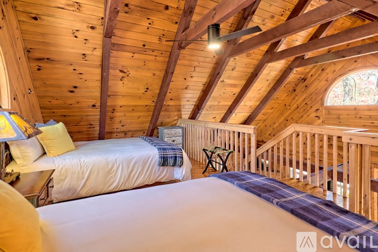 A bedroom with wooden walls and ceiling, a bed with a white comforter, and a small table with a chair.