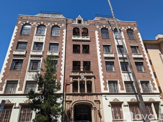 A tall red brick building with many windows and a tree in front.