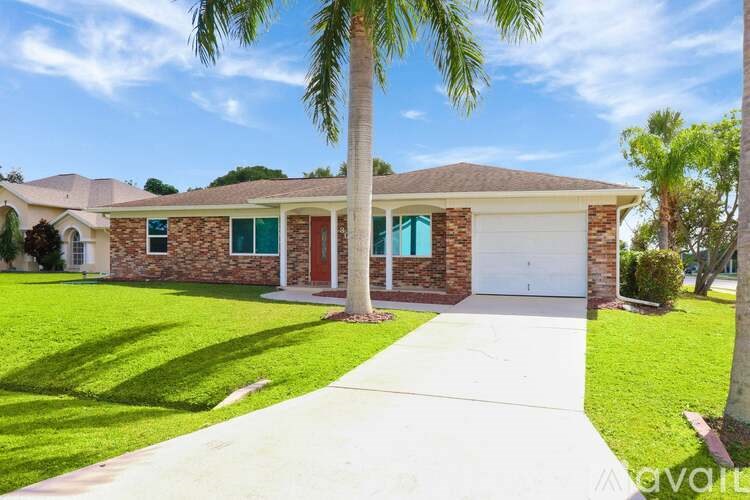 A house with a red door and a garage is surrounded by a well-manicured lawn.
