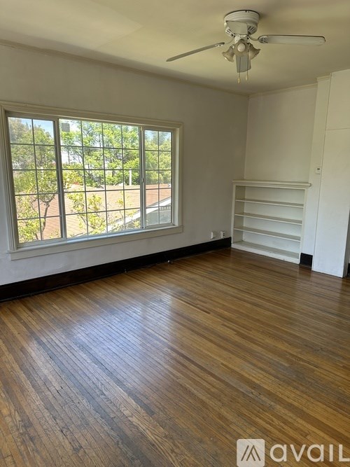 A room with wooden floors and a window overlooking a garden.