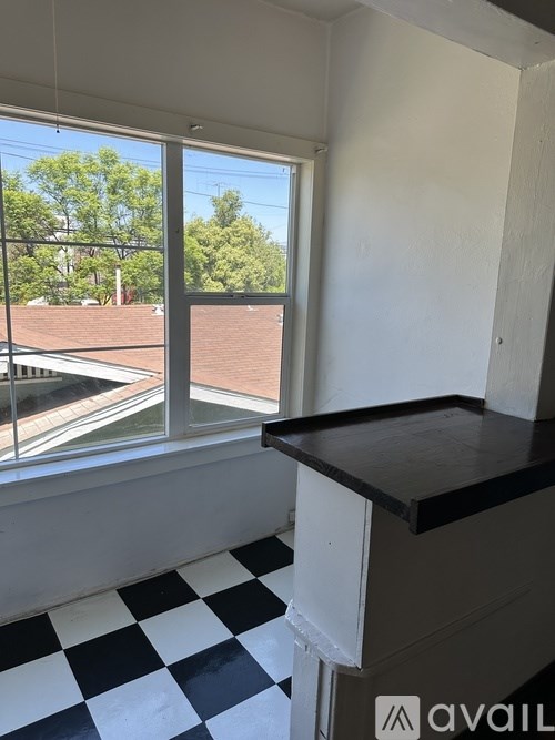 A room with a checkered floor and a window overlooking a red roofed building.