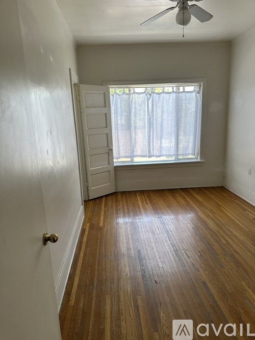 A room with wooden floors and a window with white curtains.