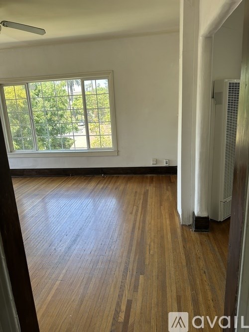 A room with wooden flooring and a window overlooking a tree-filled yard.