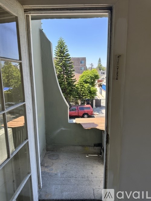 A view from inside a room looking out to a red car and a tree.