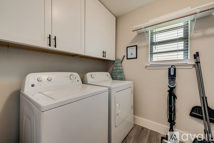A small laundry room with a washer and dryer, a vacuum cleaner, and a window with blinds.