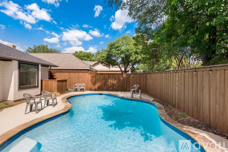 A small residential pool surrounded by a wooden fence and trees.