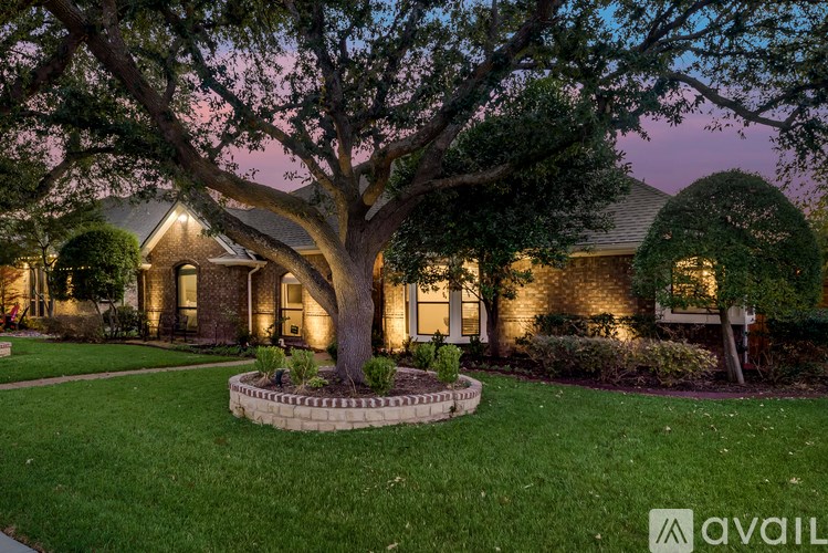 A house with a large tree in front and lights on.