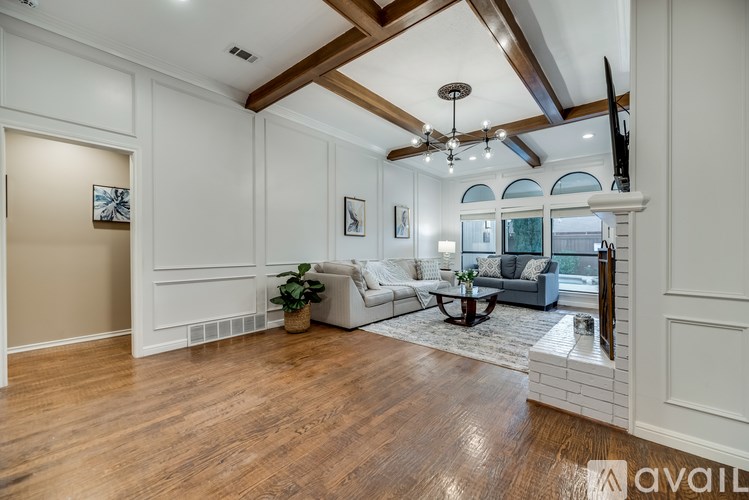 A spacious living room with a wooden floor and a high ceiling with exposed beams.