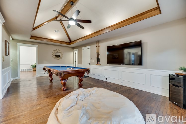 A pool table is in the middle of a room with wood floors and a ceiling fan.