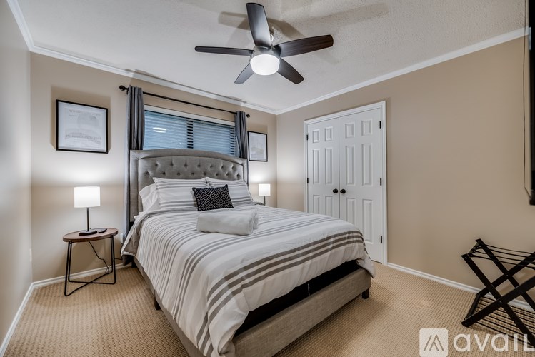 A bedroom with a large bed, a ceiling fan, and a window with blinds.