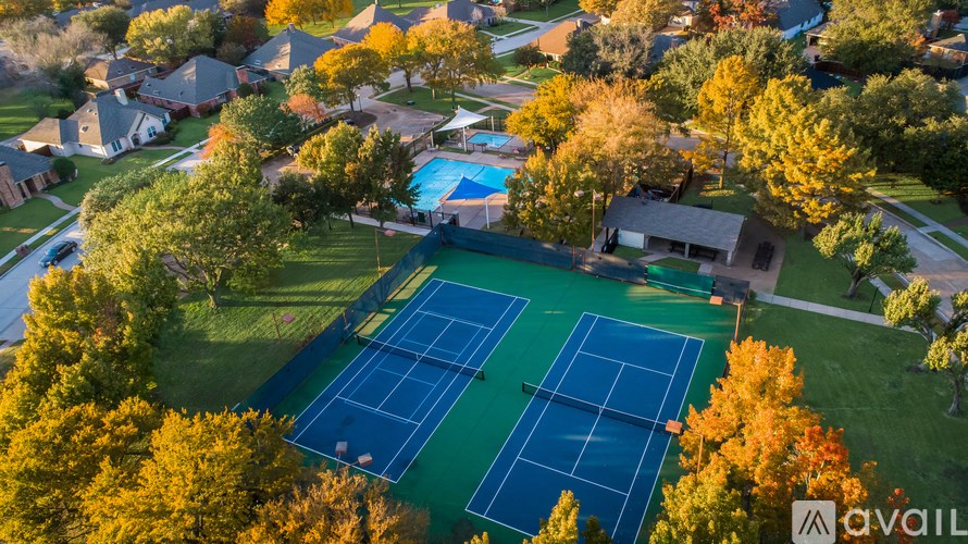 An aerial view of a tennis court surrounded by trees and houses.