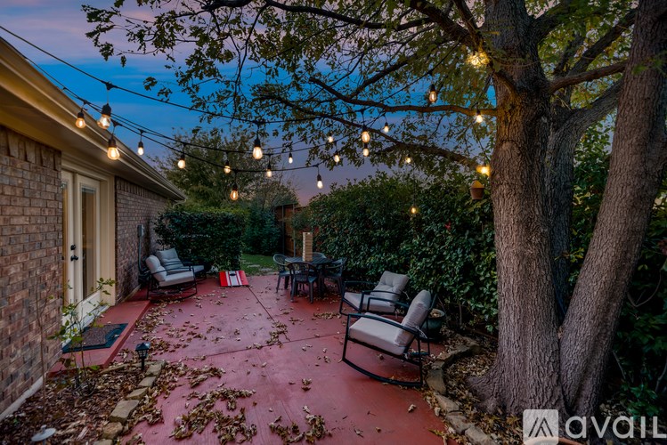 A backyard with a table and chairs under a tree with lights strung above.