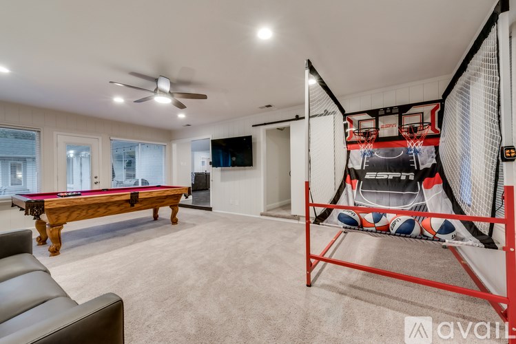 A room with a pool table, a couch, and a basketball hoop.