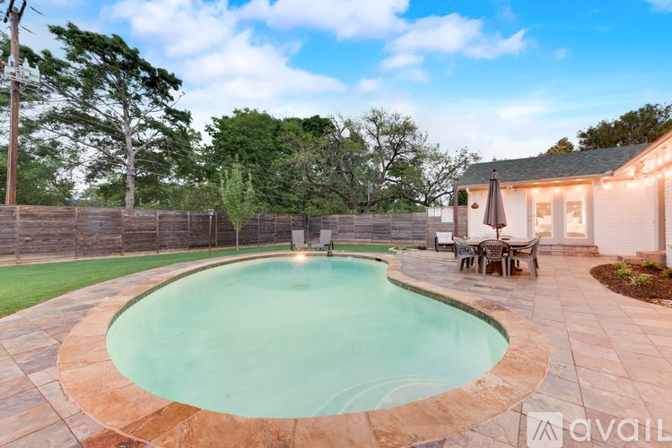 A swimming pool surrounded by a stone patio and a wooden fence.
