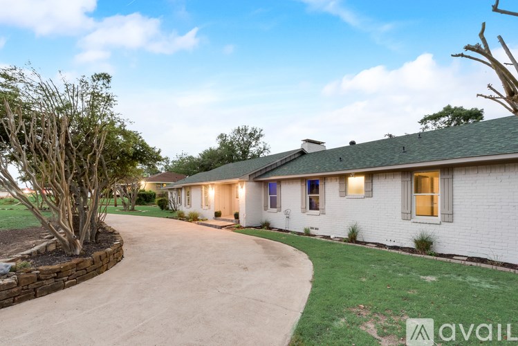 A white house with a green roof and a driveway leading to the front door.