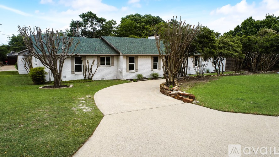A white house with a green roof is surrounded by a well-kept lawn and trees.