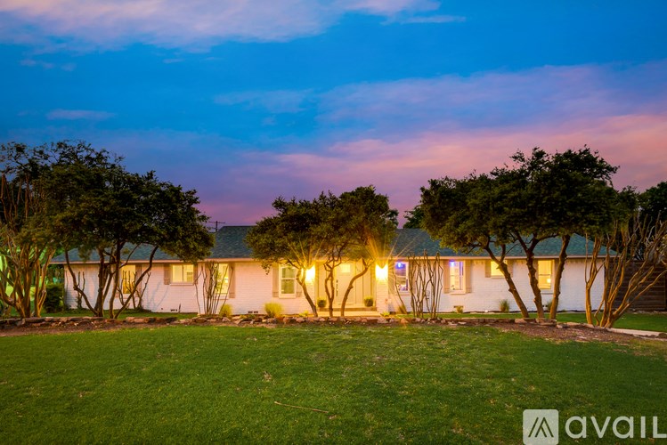 A house with a lawn and trees in front of it is lit up at dusk.