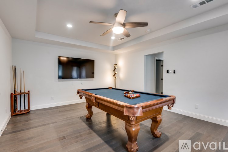 A pool table is in the middle of a room with a ceiling fan and a television mounted on the wall.