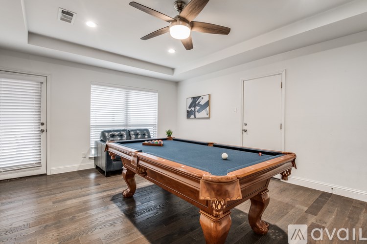 A pool table with a green cloth and white balls is in the center of a room with a ceiling fan.