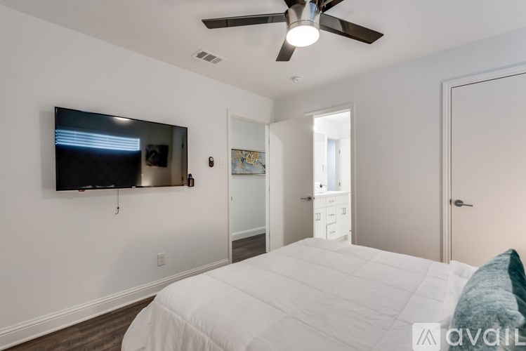 A bedroom with a bed, a ceiling fan, and a flat screen TV mounted on the wall.
