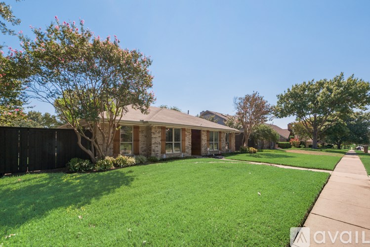 A house with a green lawn and a tree with pink flowers in front.