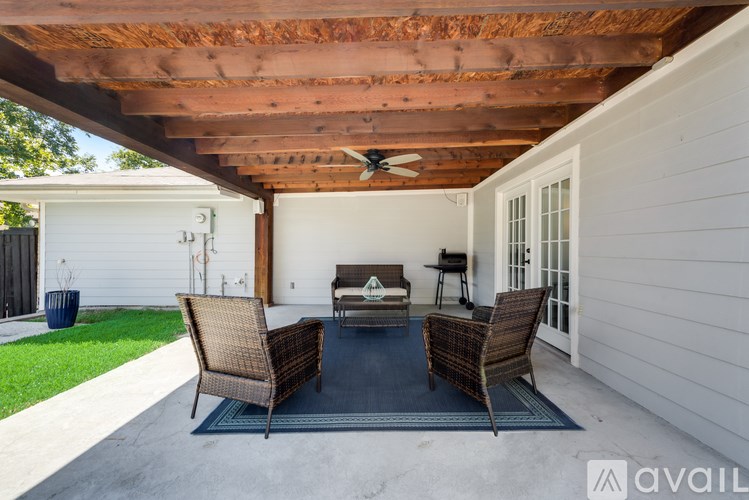 A patio with a wicker sofa and chairs under a wooden roof.